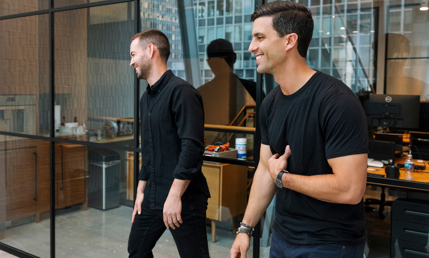 Two colleagues smiling and walking inside a modern office with glass walls.