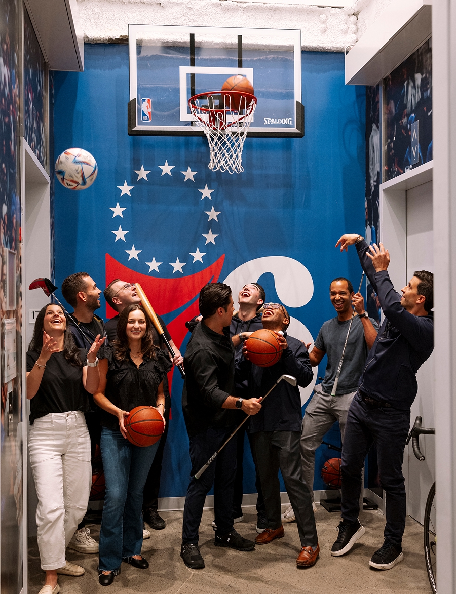 Group of colleagues laughing and playing basketball together indoors.