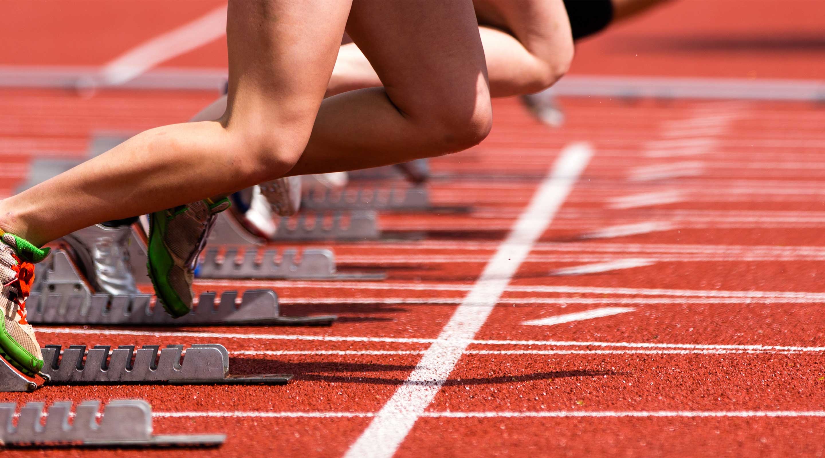 Athletes starting a sprint race on a track, pushing off from starting blocks.