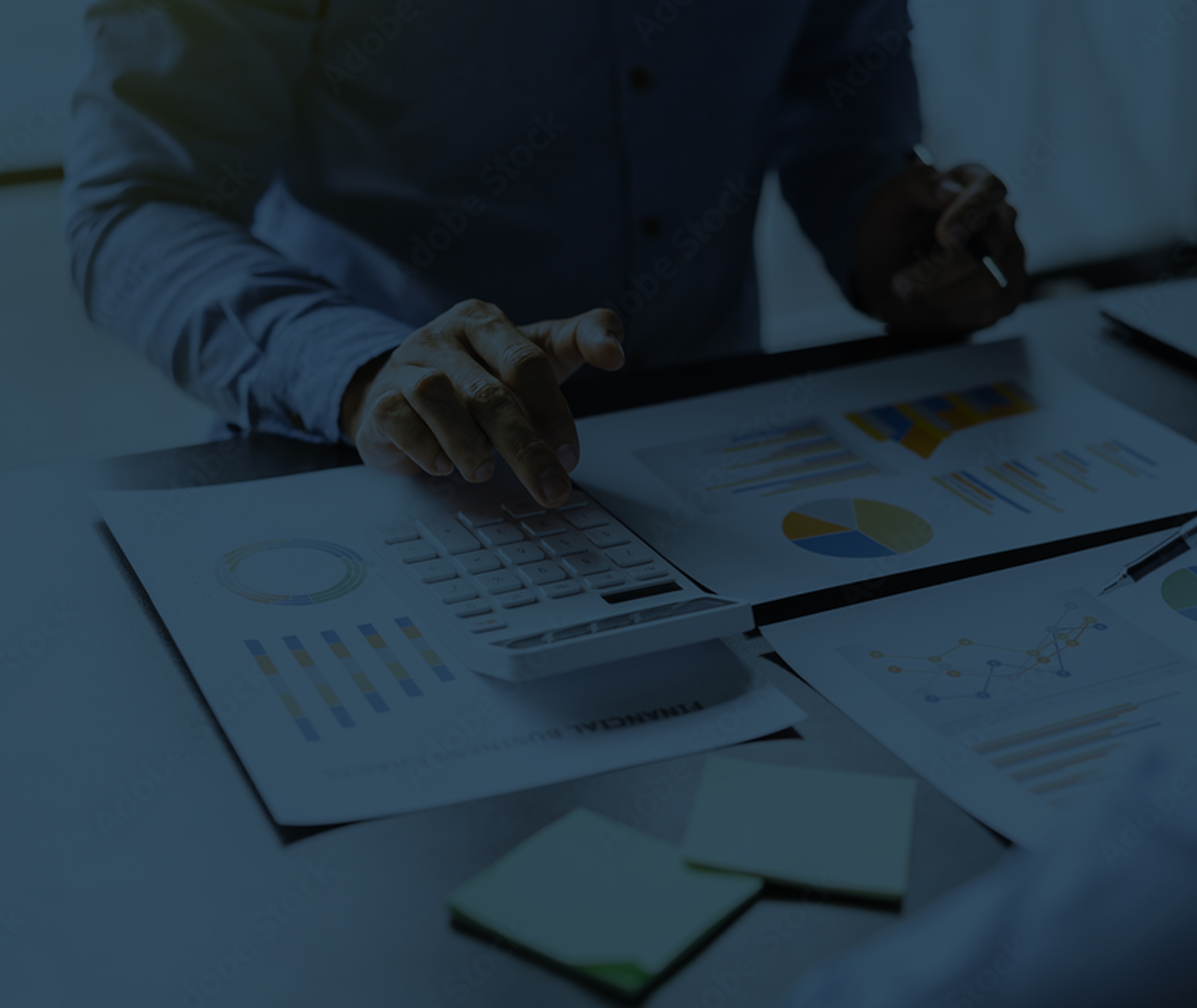 Person using a calculator and reviewing financial documents with charts and graphs on a desk.